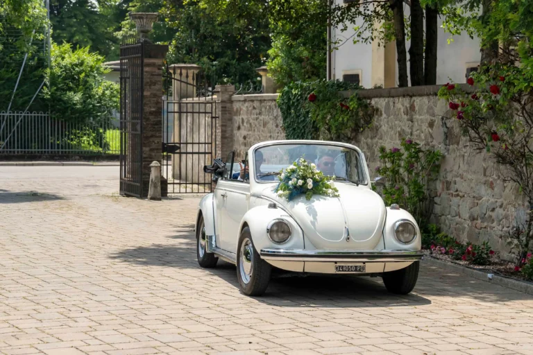 primo piano di un auto d'epoca decappotabile bianca con mazzo di fiori sopra il cofano che entra in un viale murato