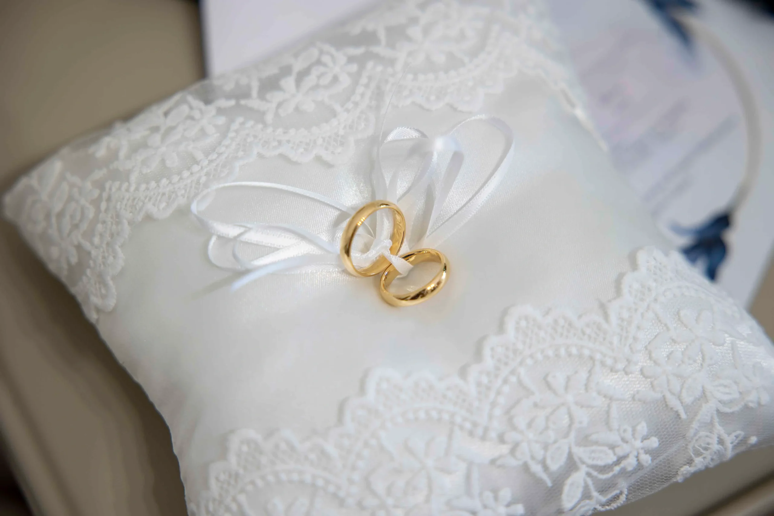 Primo piano di due fedi nuziali appoggiate su un cuscino bianco finemente decorato con pizzo, simbolo elegante e romantico dell’unione matrimoniale.