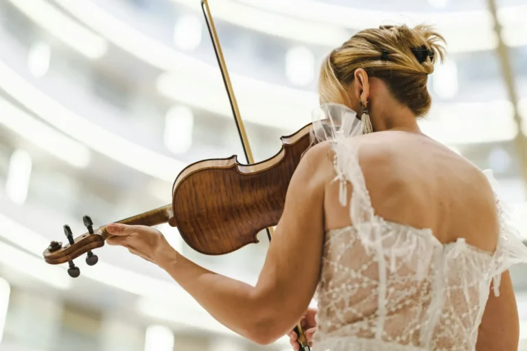 Primo piano di donna in abito elegante bianco che suona il violino inquadrata di spalle