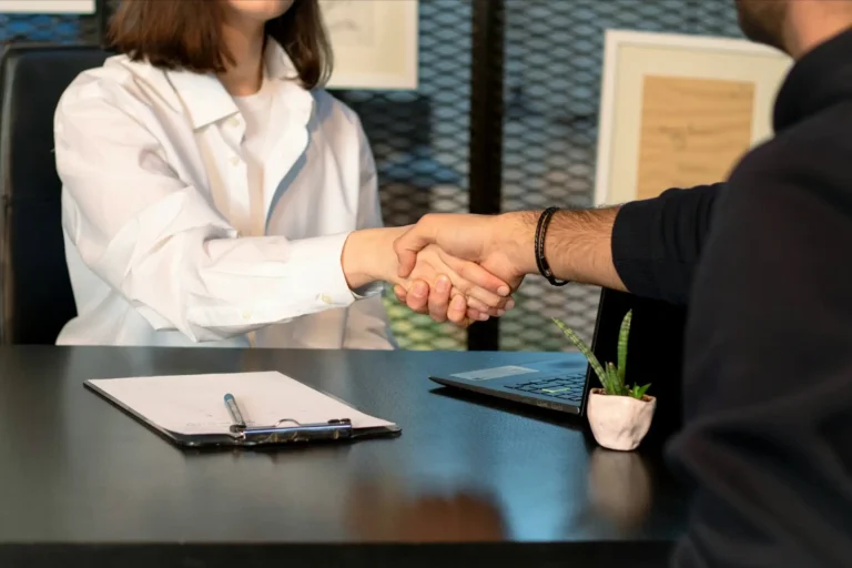 Due persone sedute alla scrivania che si stringono la mano